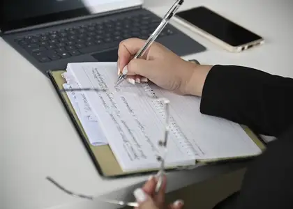 Une main note quelques lignes sur un bloc, à côté d'un ordinateur portable