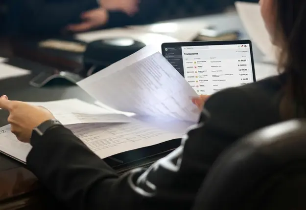 Une personne compare une pièce du dossier au relevé des opérations affiché sur un ordinateur portable